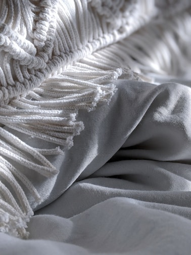 A cozy folded pink textile blanket with subtle embroidery on a light gray background.