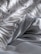Close-up of a textured blanket or fabric with intricate woven patterns and fringes on a smooth surface, showing soft folds and subtle shadows.