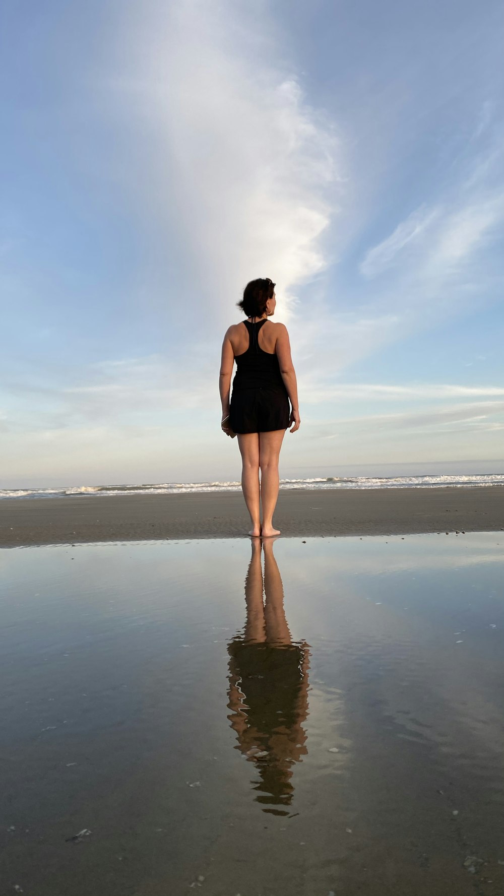 woman in black mini dress standing on seashore during daytime