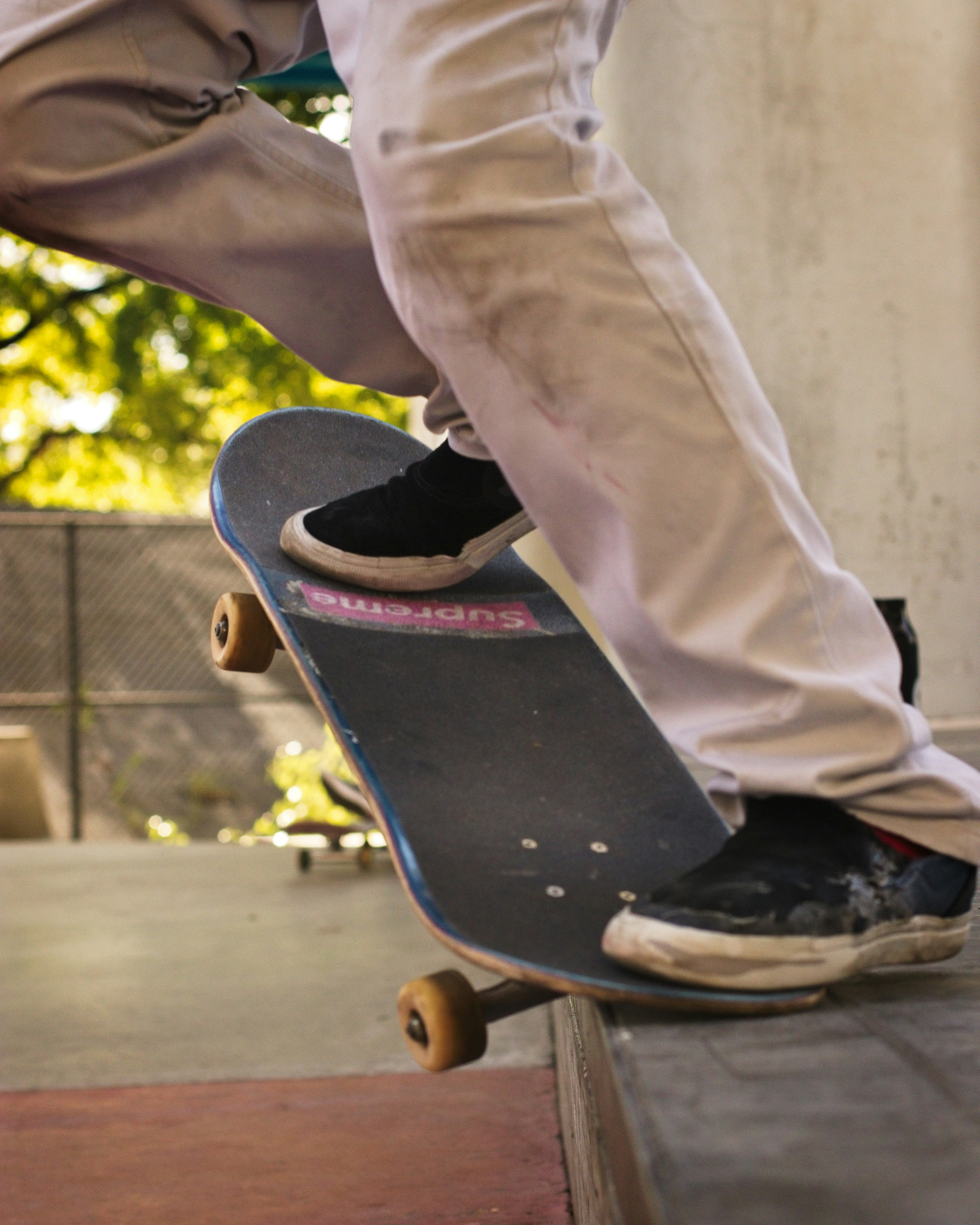 person in white pants and black and white nike sneakers sitting on black and red skateboard