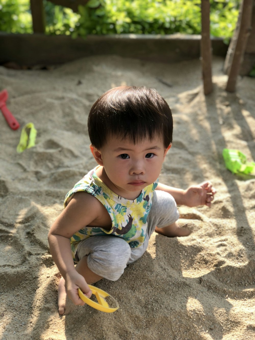 boy in white and red stripe tank top sitting on brown sand during daytime