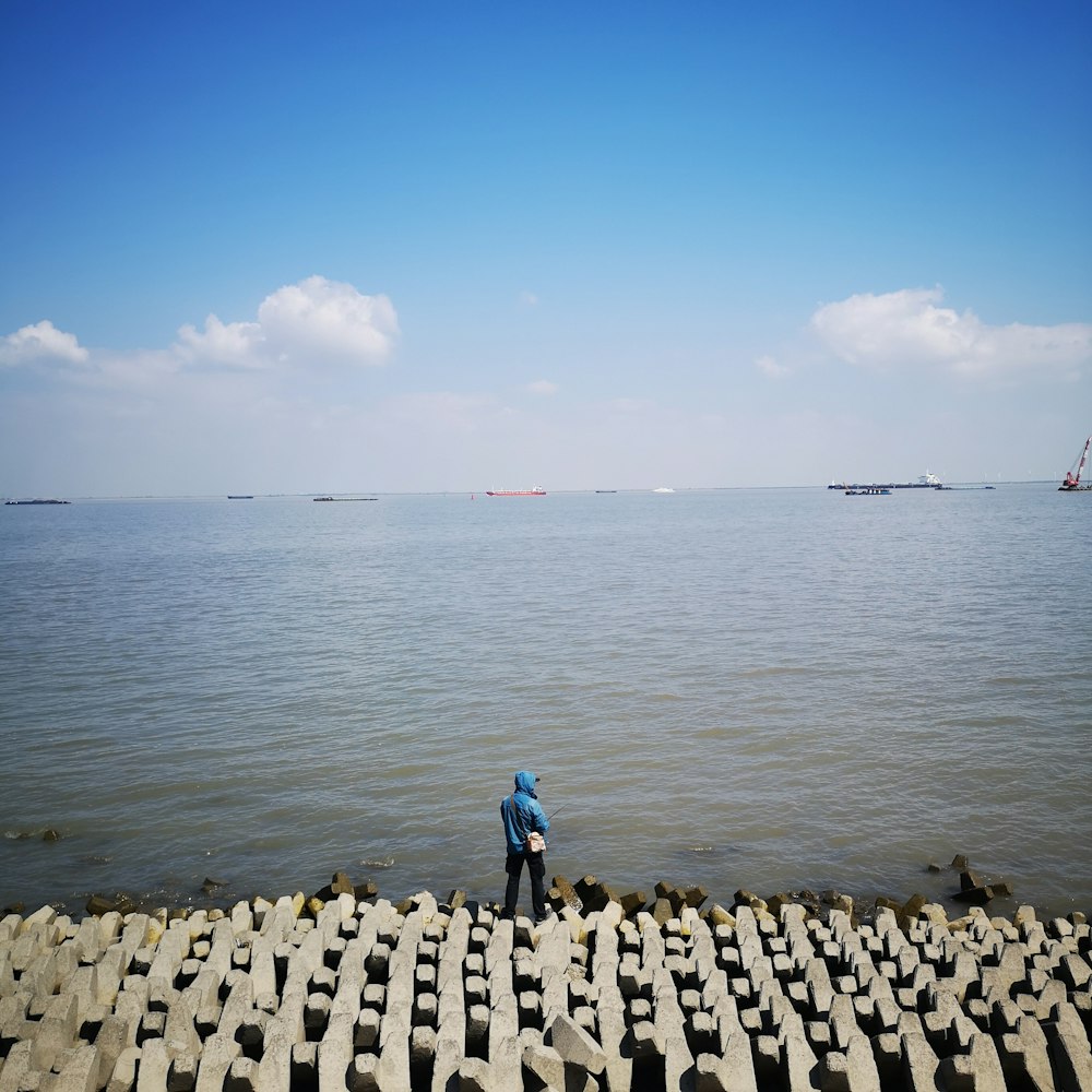 person in blue jacket walking on gray concrete pathway near body of water during daytime