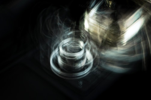 Swirling abstract shapes and blurred light create a sense of motion and energy. The image has a dark background with a central circular form that appears to be glowing, creating a dynamic and mysterious feeling.