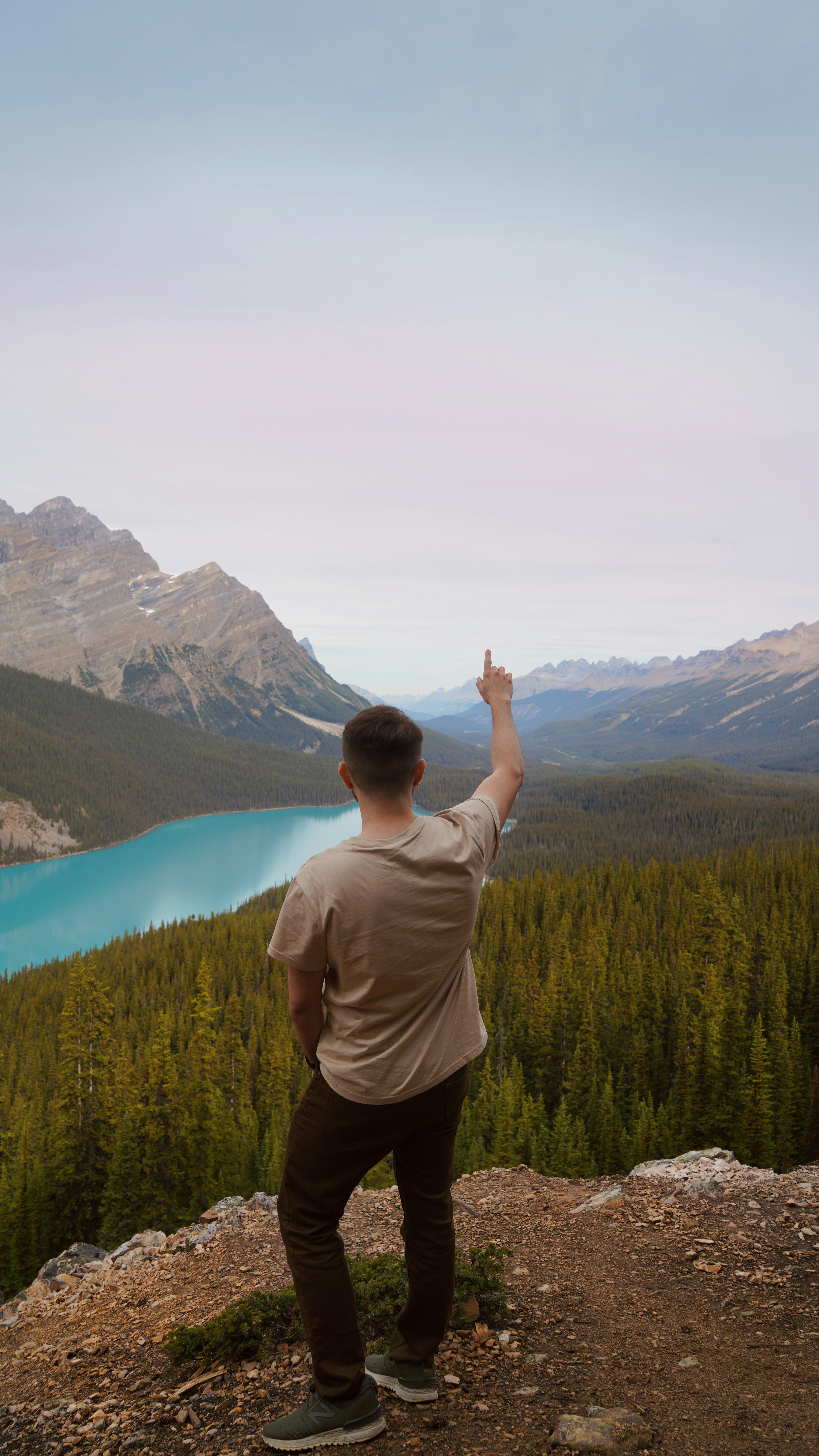a man standing on top of a mountain pointing at a lake