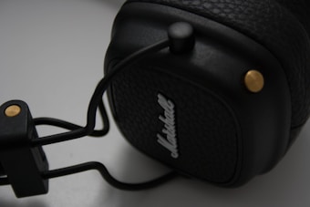 A close-up view of a black leather-textured headphone with gold accents. The brand name is embossed on the ear cup. The focus is primarily on the ear cup, showing the intricate details of the leather texture and metal components.