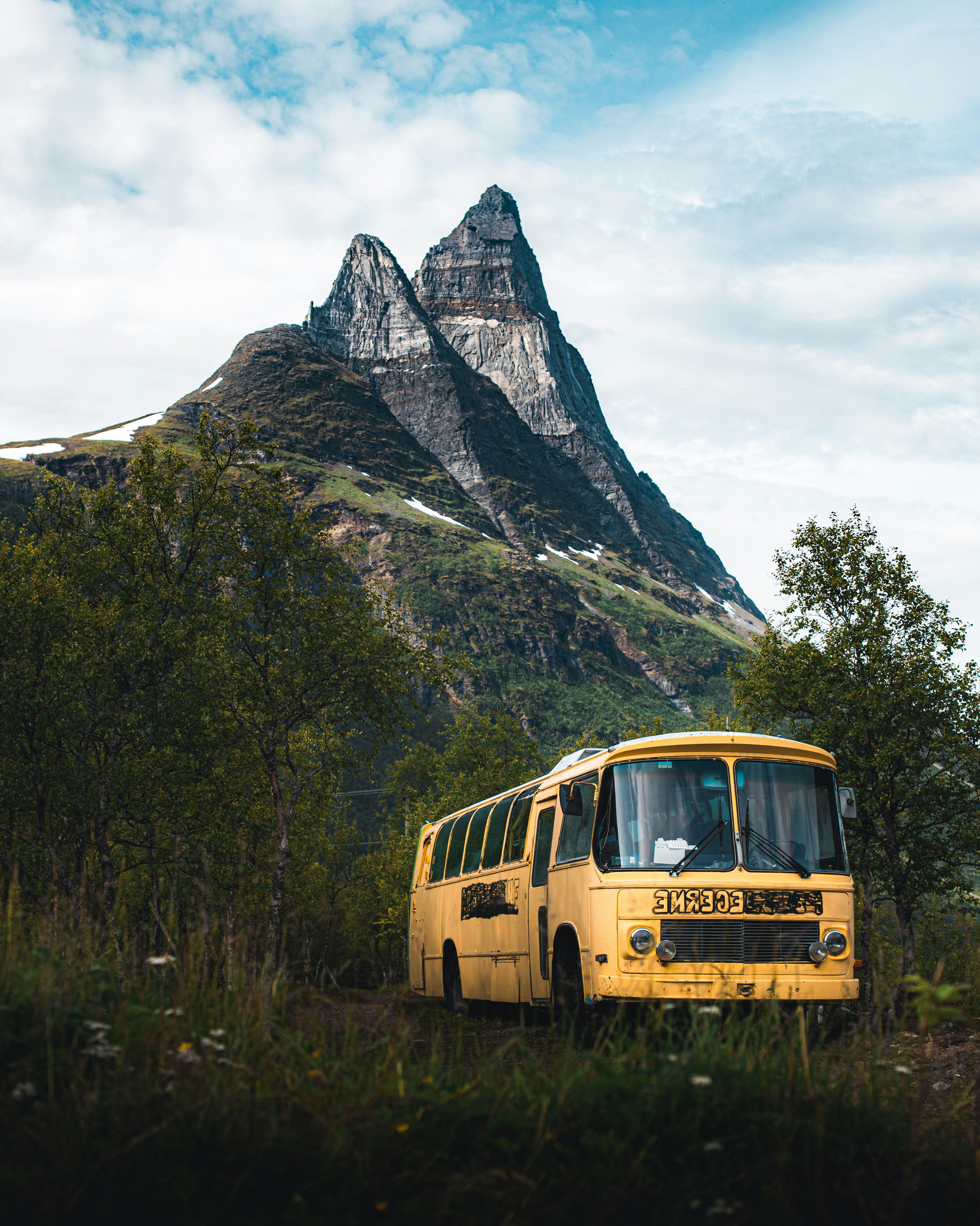 A yellow bus parked on a green grassy slope below a mountain — the kind of cross-country route where Culture Brawl prompts get tested in real time