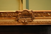 An ornate, decorative picture frame featuring intricate floral and leaf patterns with a small plaque in the center that displays the name 'P. Rembrandt' in both Latin and Cyrillic scripts.