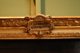 An ornate, decorative picture frame featuring intricate floral and leaf patterns with a small plaque in the center that displays the name 'P. Rembrandt' in both Latin and Cyrillic scripts.