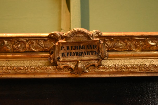 An ornate, decorative picture frame featuring intricate floral and leaf patterns with a small plaque in the center that displays the name 'P. Rembrandt' in both Latin and Cyrillic scripts.