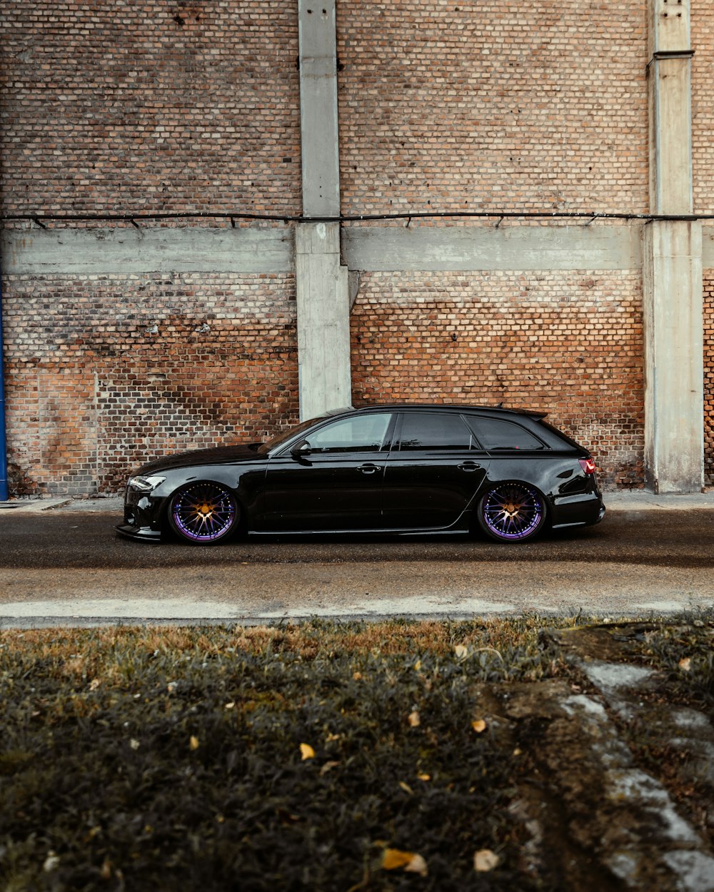 black sedan parked beside brown brick wall