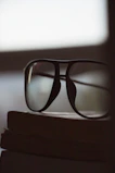 Minimalist black-rimmed glasses resting on an open book with soft morning light.