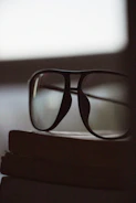 Minimalist black-rimmed glasses resting on an open book with soft morning light.