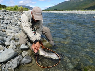 Two anglers celebrating a big catch together on a sunny riverbank.