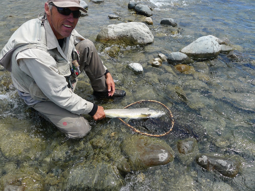 Hombre con chaqueta gris y pantalones negros sosteniendo peces