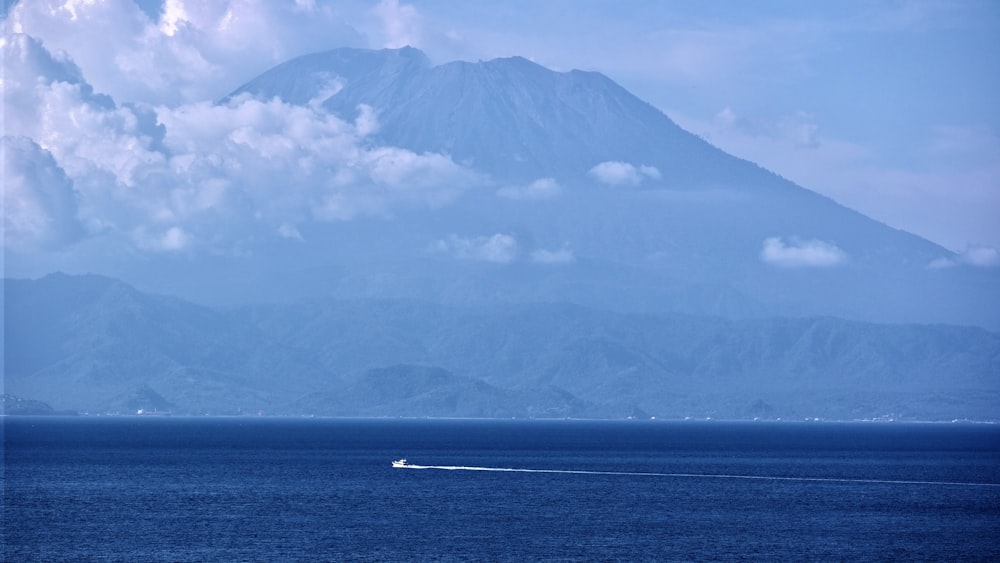 body of water near mountain under white clouds during daytime