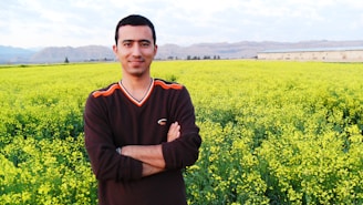 Justin Canelas standing in a lush Kaʻū farm field, smiling warmly with mountains in the background.