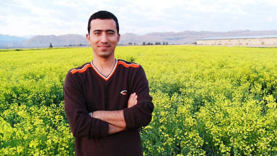 Justin Canelas standing in a lush Kaʻū farm field, smiling warmly with mountains in the background.