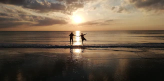 A vibrant circle of people dancing joyfully on a beach at sunset, surrounded by nature.