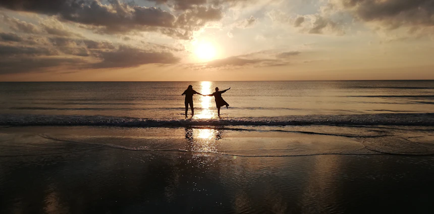 A vibrant circle of people dancing joyfully on a beach at sunset, surrounded by nature.