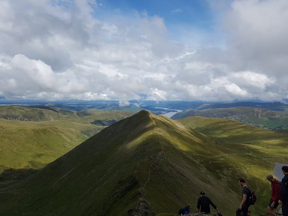 Persone in piedi sul campo di erba verde vicino alla montagna sotto nuvole bianche durante il giorno