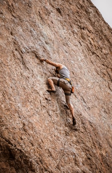 woman in gray sports bra and black shorts climbing on brown rock mountain during daytime
