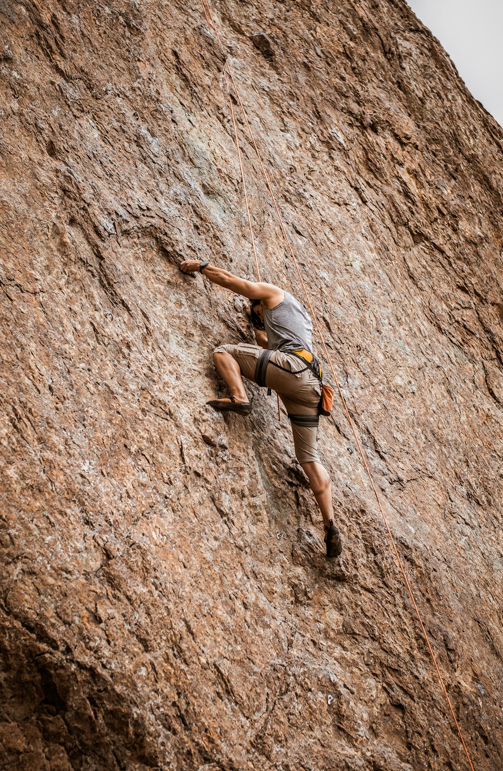 mulher no sutiã esportivo cinza e shorts pretos escalando na montanha de rocha marrom durante o dia