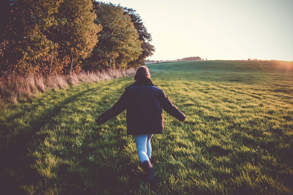 woman in black jacket and blue denim jeans standing on green grass field during daytime