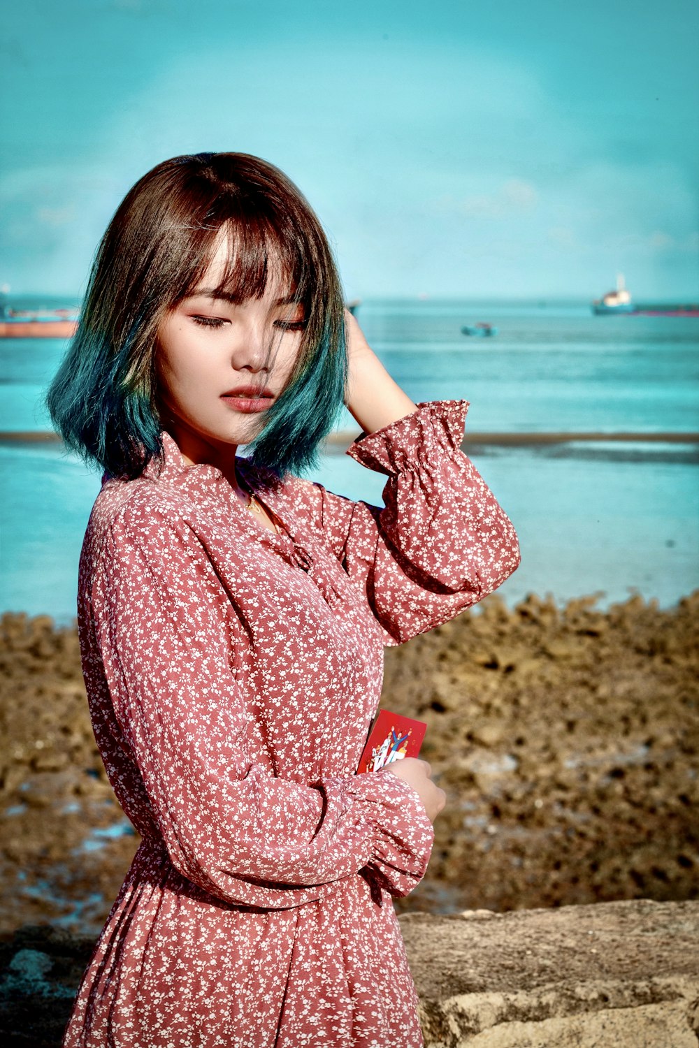 woman in pink sweater standing on brown sand near body of water during daytime