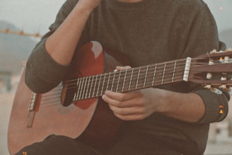 man in gray crew neck t-shirt playing brown acoustic guitar