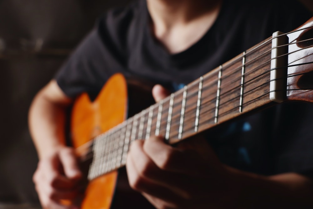 Hombre con camisa negra de manga larga tocando la guitarra acústica marrón