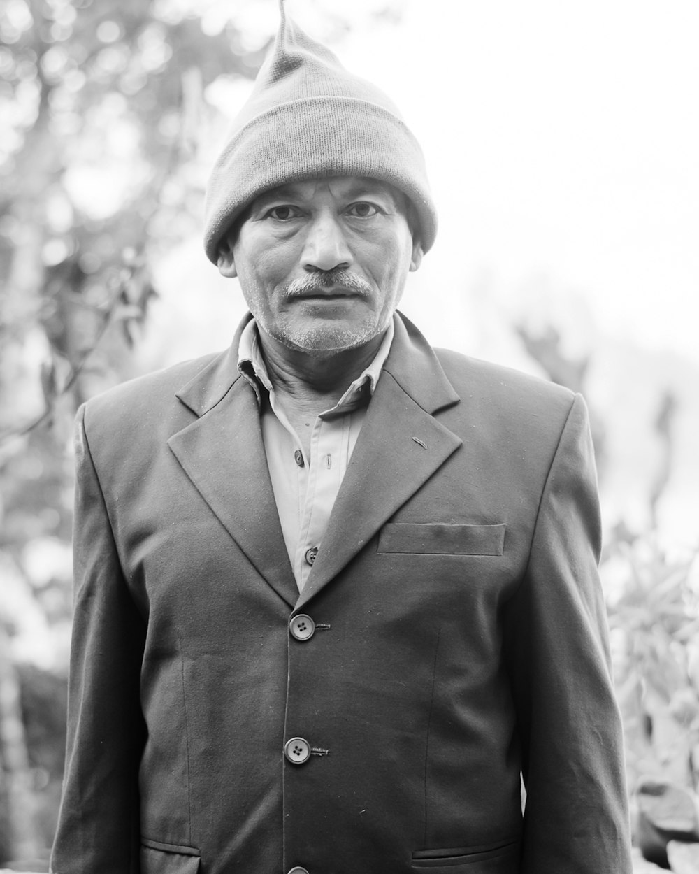 man in black suit jacket and knit cap in grayscale photography