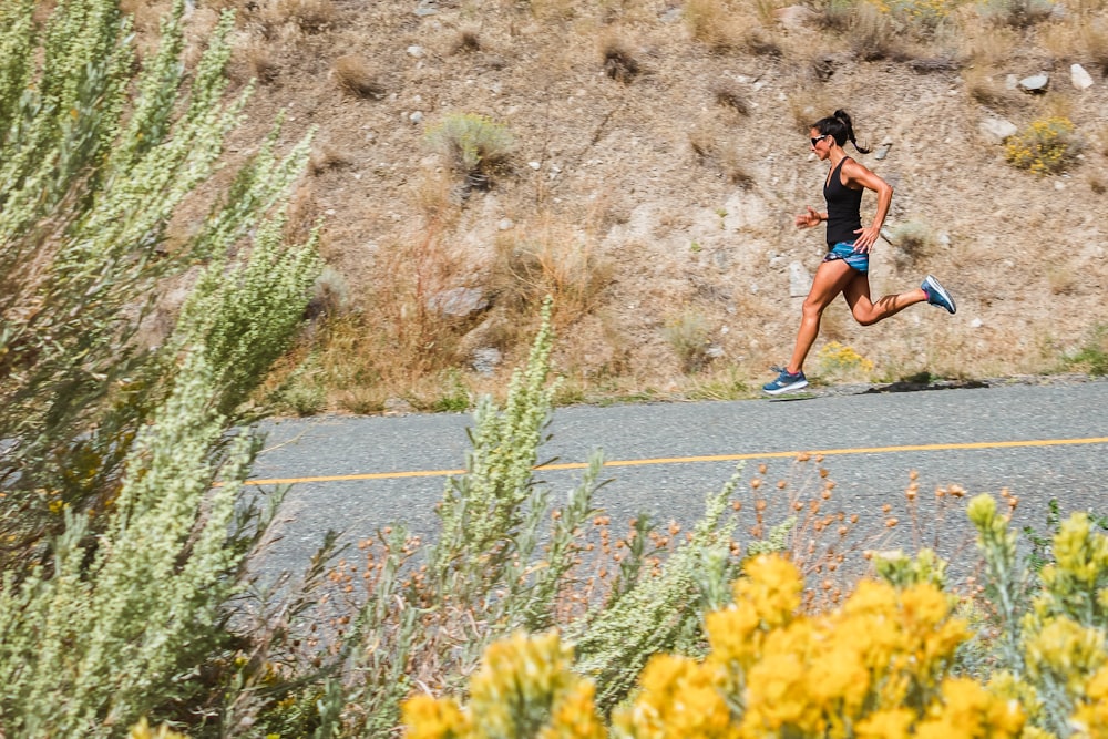 woman in black tank top running on gray asphalt road during daytime