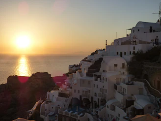 Elegant Mediterranean coastline at sunset with soft white buildings and golden light reflecting on the sea.