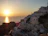 Sunset over a vibrant Mediterranean coastal village with colorful houses and palm trees.