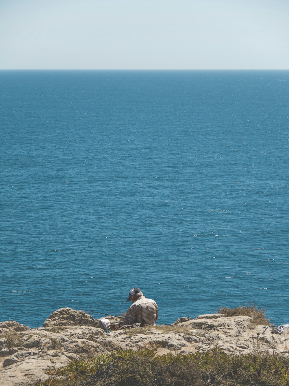Mann im grauen Hemd sitzt tagsüber auf Felsen in der Nähe von Gewässern