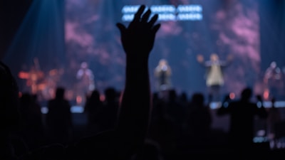 Close-up of a hand raising a ticket stub against a backdrop of pulsing speakers.