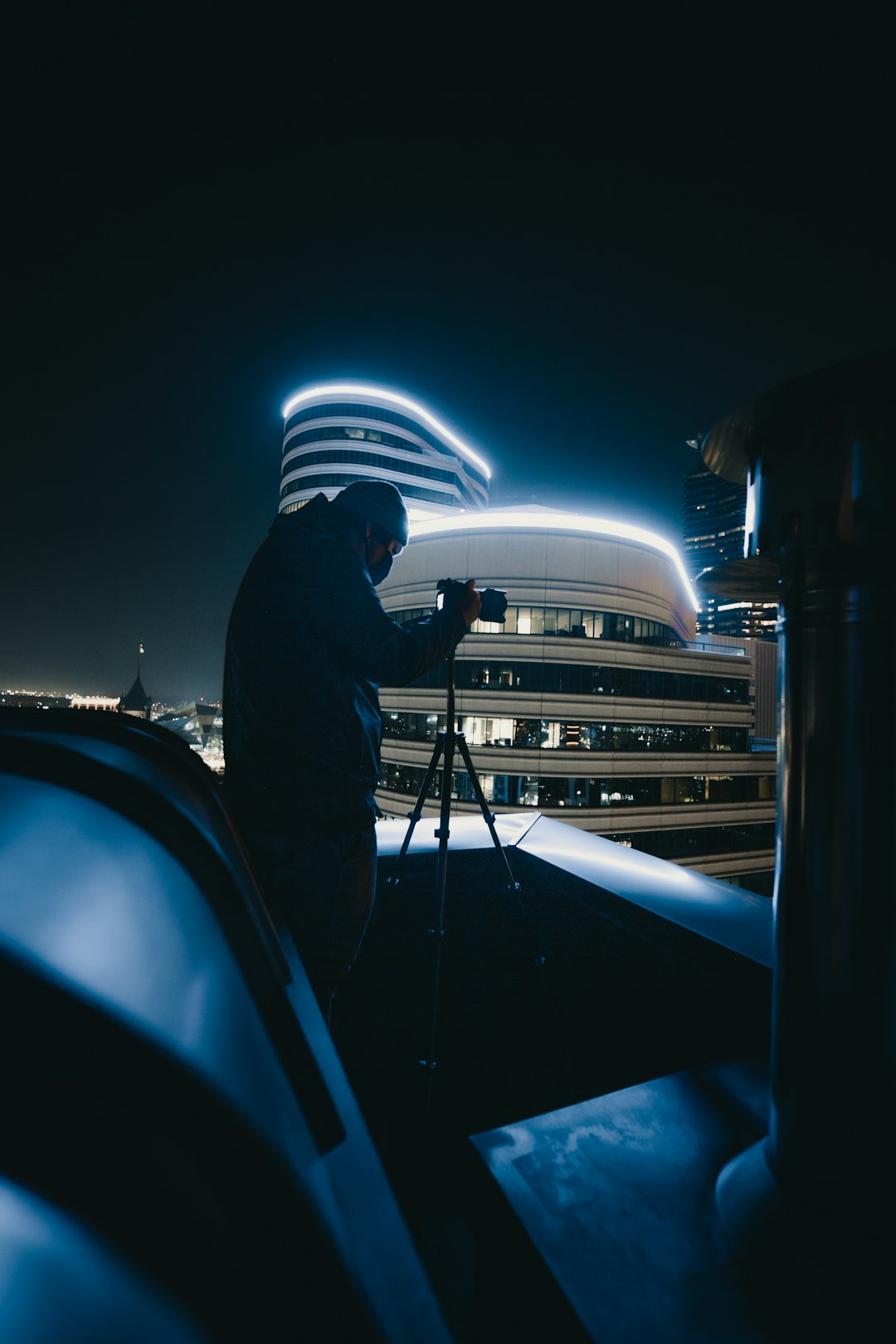 man in black jacket standing near blue car during night time