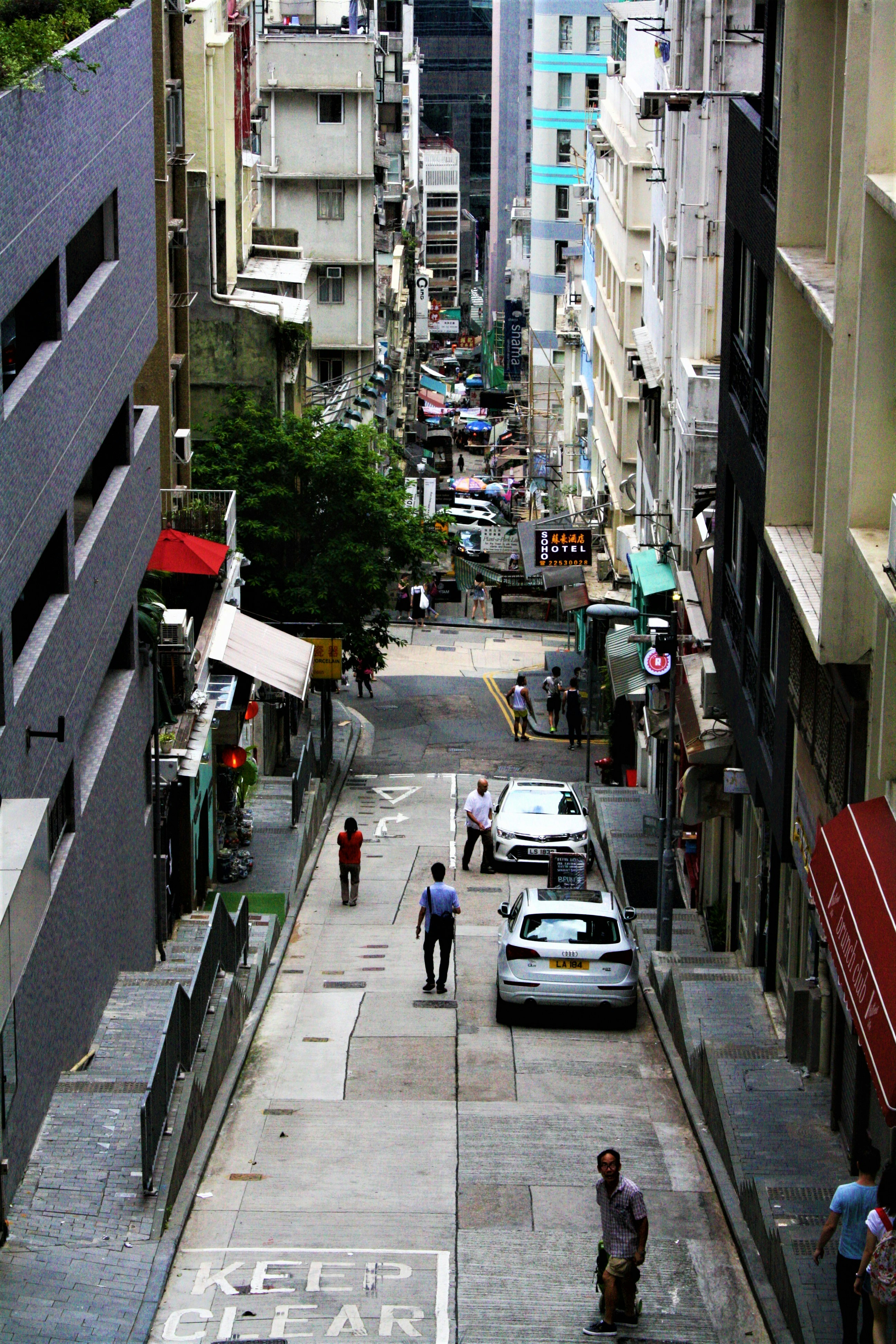 people walking on sidewalk near cars parked on sidewalk during daytime