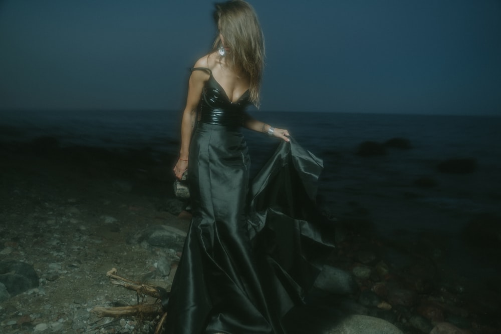 낮 동안 해변 해변에 서 있는 검은 민소매 드레스를 입은 여자
