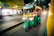 A green and yellow auto rickshaw with passengers is moving swiftly down a street at night, with blurred shops and streetlights in the background indicating the vehicle's speed.