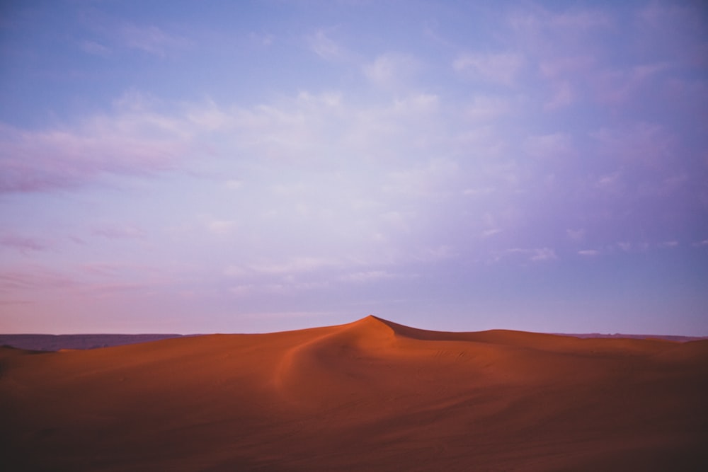 brown sand under white clouds and blue sky during daytime