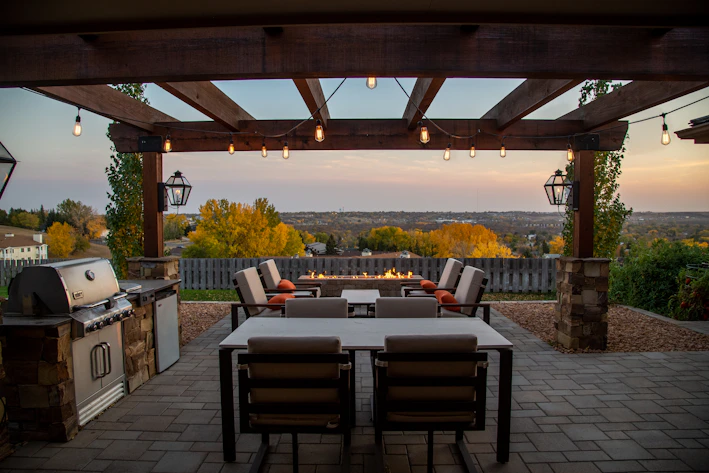 A cozy outdoor patio shaded by a sleek black pergola with red accents.