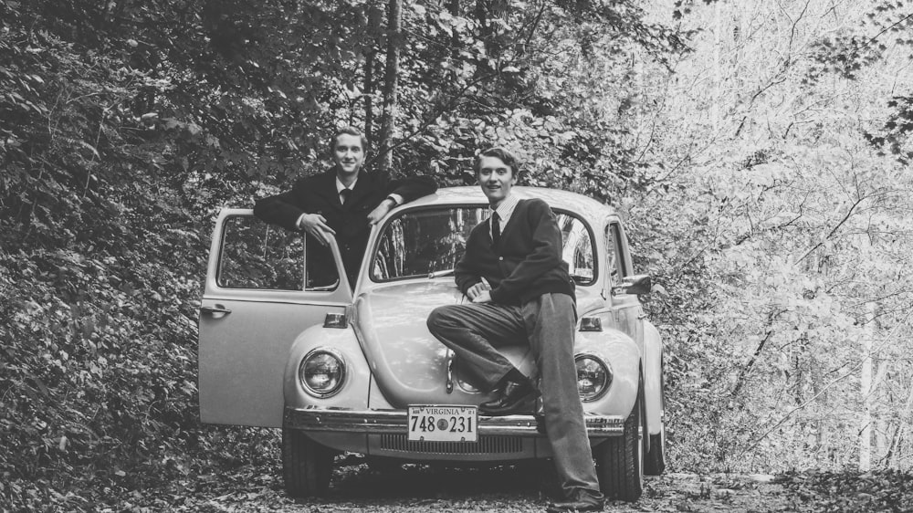 grayscale photo of man in black jacket sitting on car