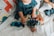 A toddler sits on a bed playing with a colorful guitar-shaped toy. The toy features bright buttons and interactive elements. The child is wearing a dark teal outfit and is surrounded by playful, animal-themed bedding with images of llamas and monkeys.