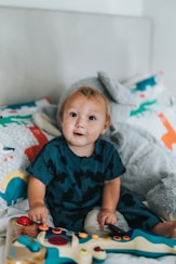 child in blue and red button up shirt sitting on bed