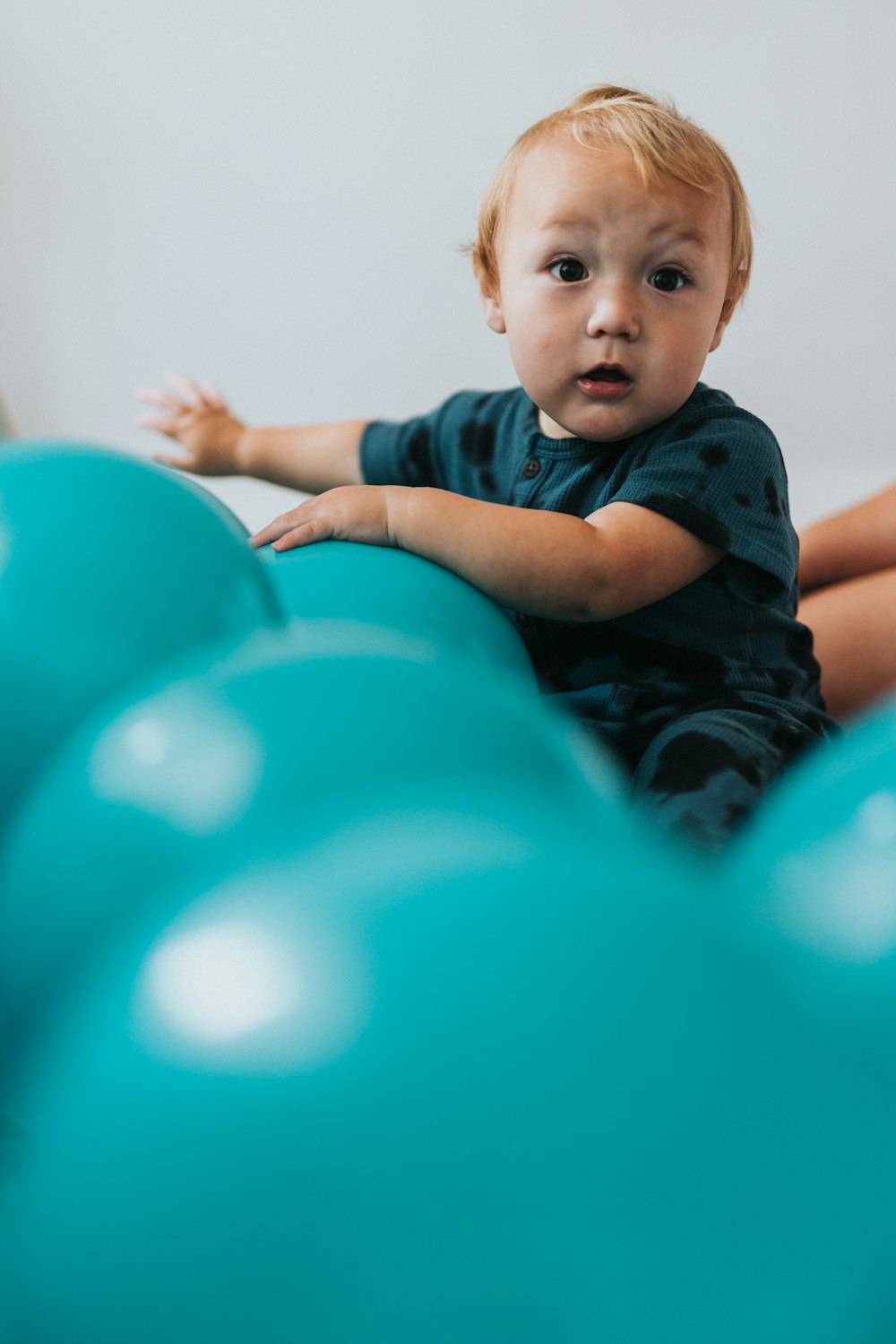 boy in blue and black stripe polo shirt lying on blue inflatable balloons
