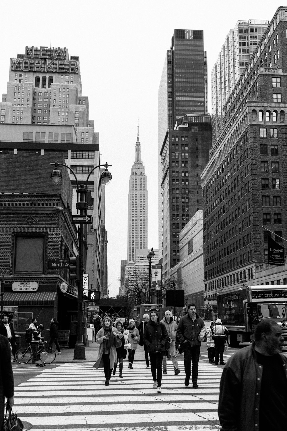 grayscale photo of people walking on street near high rise buildings