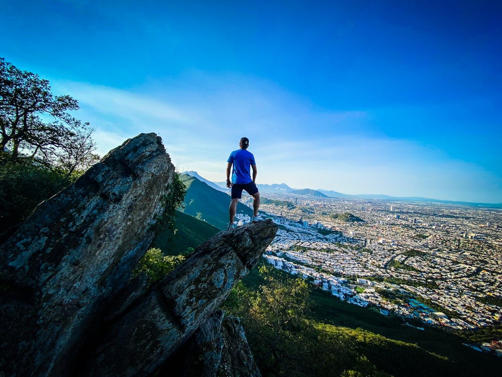 man in blue t-shirt standing on rock during daytime