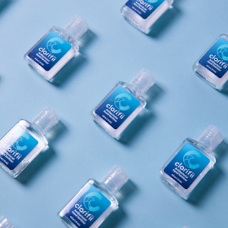 Several small bottles of hand sanitizer with blue labels are arranged on a light blue background in a diagonal pattern.