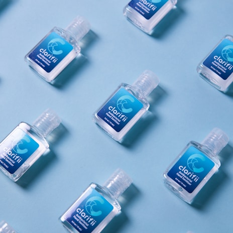 Several small bottles of hand sanitizer with blue labels are arranged on a light blue background in a diagonal pattern.